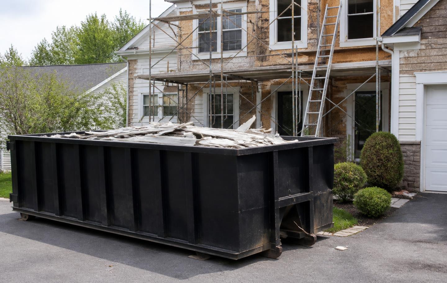Roll-off dumpster full of siding debris at a house exterior remodel with scaffolding