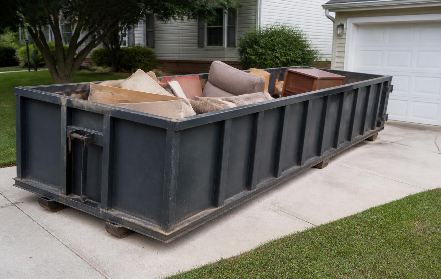 20-yard roll-off dumpster on a driveway holding furniture and carpet from a home cleanout